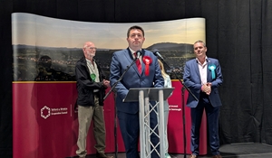 A picture of Shaun Davies standing at a lectern on election night, making a speech as the newly elected MP for Telford, with the other party candidates standing behind him.