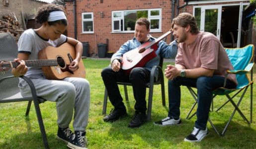 Girl playing guitar on left, man sat holding guitar, and young man watching on right