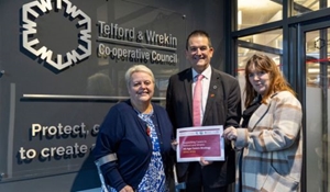 Cllrs Shirley Reynolds, Paul Watling and Kelly Middleton display cover of the All Age Carers Strategy in front of council signage