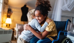 An older child sitting in a wheelchair and smiling while she hugs a younger child