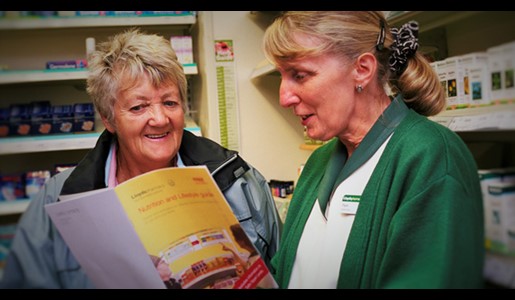 Woman speaks to pharmacy worker who is showing her an information leaflet