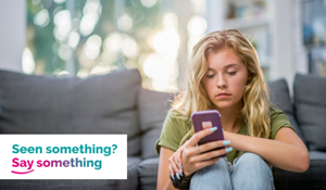 A teenager sitting on the floor in a house, scrolling on a mobile phone. A graphic says Seen something Say something.