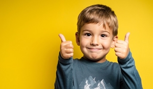 A young boy smiling with both thumbs up