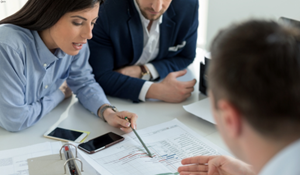A group of professionals sitting a a desk, reviewing documents together during a business meeting. This image reflects collaboration and business support