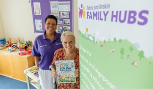 Two women smiling next to a Telford and Wrekin Family Hubs banner, with one holding a Family Fun Day flyer.