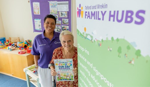 Two women smiling next to a Telford and Wrekin Family Hubs banner, with one holding a Family Fun Day flyer.