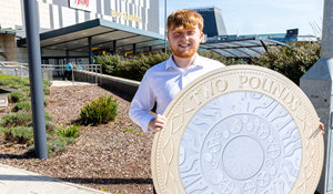 Cllr Ollie Vickers holds £2 coin in front of Telford bus station