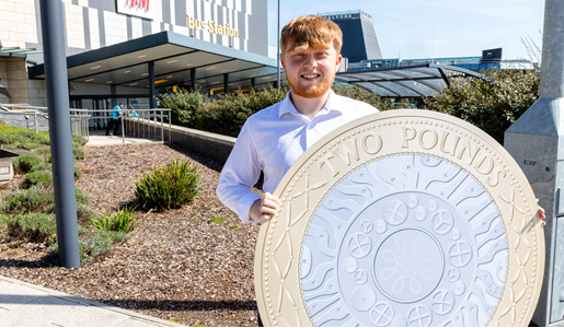 Cllr Ollie Vickers holds £2 coin in front of Telford bus station