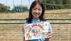 A young girl holding a hand-drawn poster supporting the England football team in front of a football goal net.