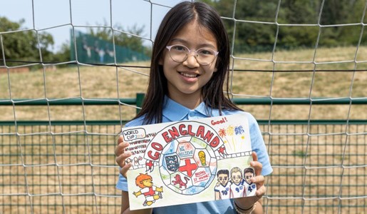 A young girl holding a hand-drawn poster supporting the England football team in front of a football goal net.