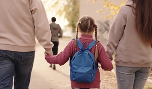 A rear view of a child with a backpack holding hands with two adults