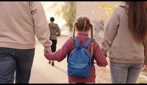A rear view of a child with a backpack holding hands with two adults