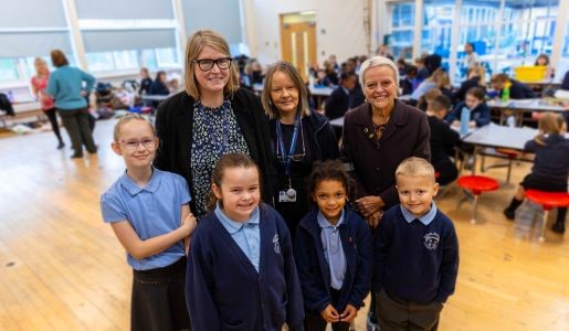 Group photo of staff and Shirley with staff and children at William Reynolds Primary School
